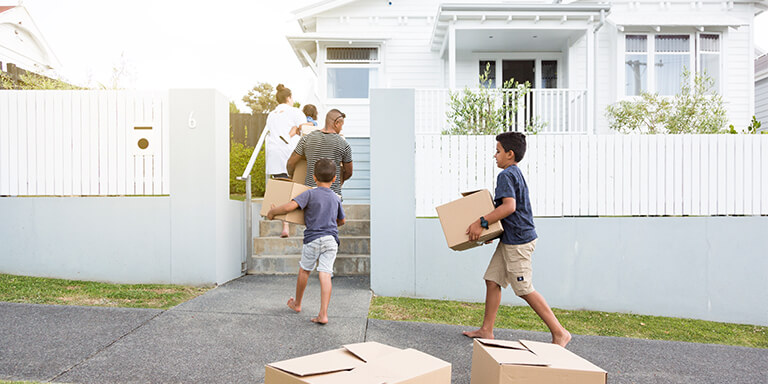 Family carrying moving boxes up the stairs into their new home