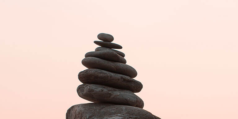 A cairn of black rocks against a light pink sky