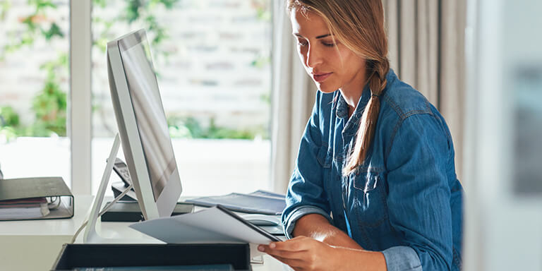 A woman sitting at a desk in front of a computer reading documents in a packet