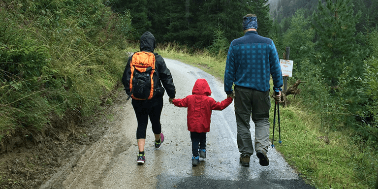Parents in hiking gear walking with their young child on a trail in the forest in the rain