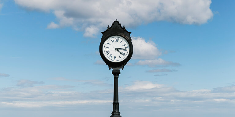 A black post clock against a blue sky background 