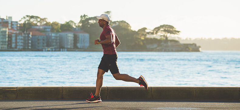 A man in athletic wear and a hat running along the edge of the waterfront