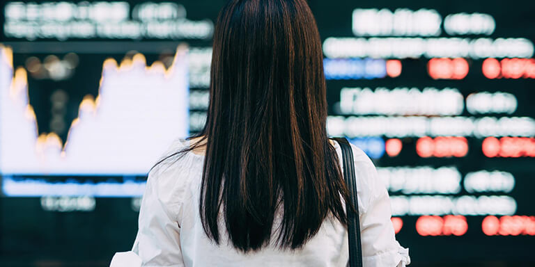 The back of a woman's head who is reading a board with stock information and rates