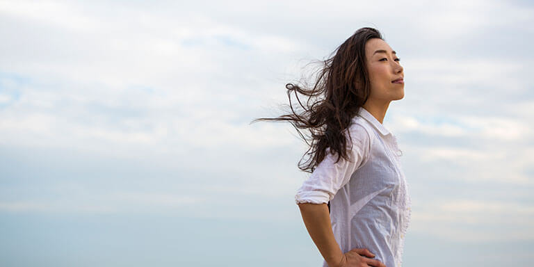 A women standing with her hands on her hips, her face turned upwards as the wind blows through her hair