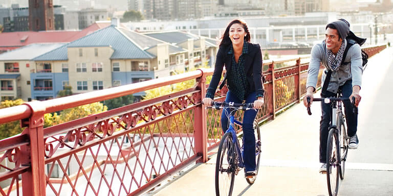 A man and woman laughing and riding their bikes along a red bridge in a city 