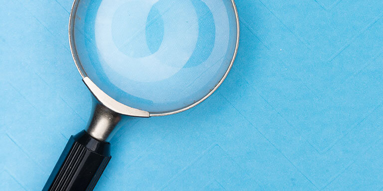 Close up of a metal magnifying glass against a sky blue background