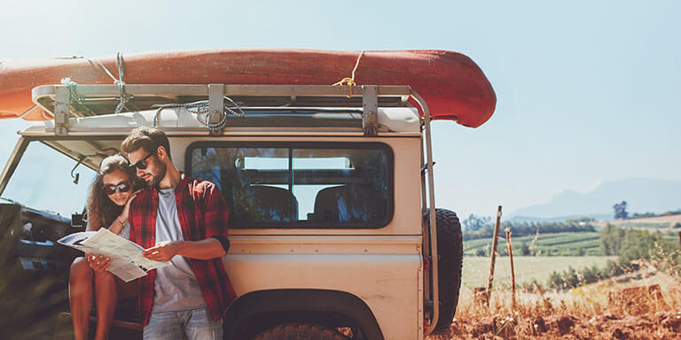 A man and a woman studying a map outside of their car in the countryside