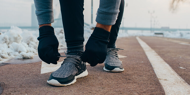 A man wearing winter athletic clothes tying his shoelaces on a running track covered in snow