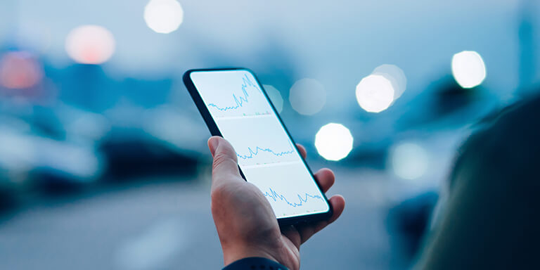 A closeup of a person looking on the smart phone at a photo of stock market charts