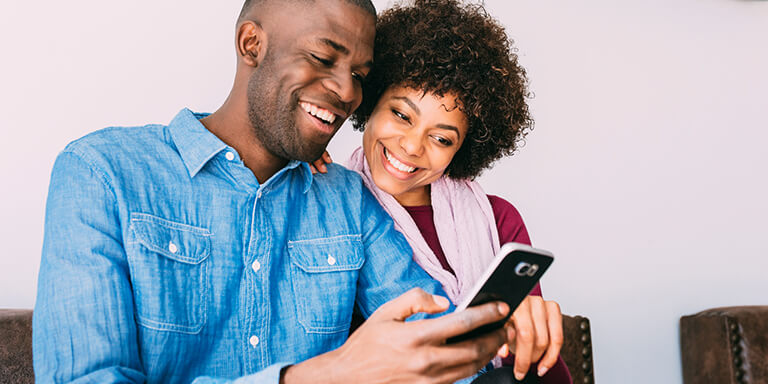 A young couple looking at something on their cellphone and smiling 
