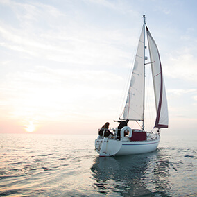 Two men on a sailboat in open waters at sunrise
