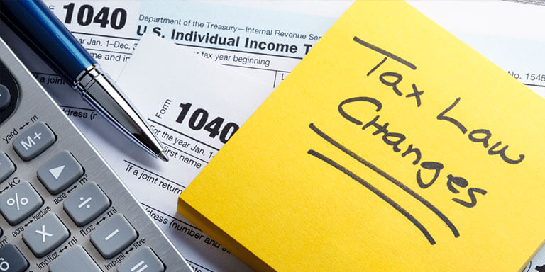 Close-up of a calculator, a pen, a 1040 form, and a yellow colored paper saying "Tax Law Changes"