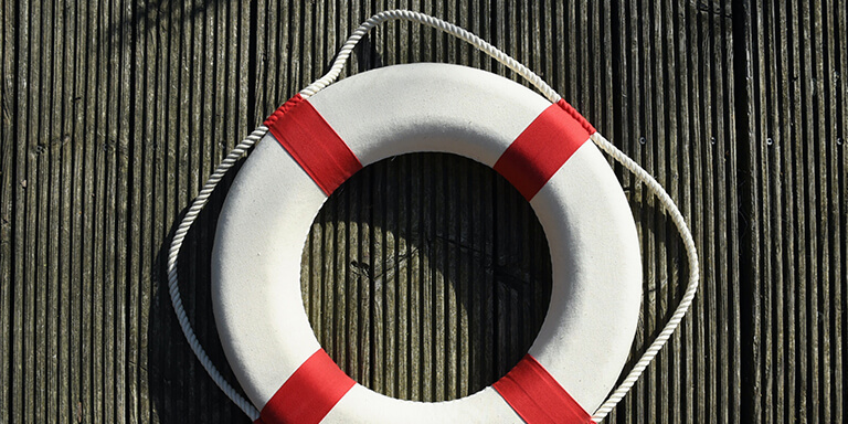 A red and white life guard ring hanging on a wooden wall 