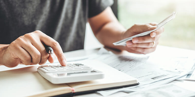 A man inputting number into his calculator while holding a pen and a stack of receipts. 