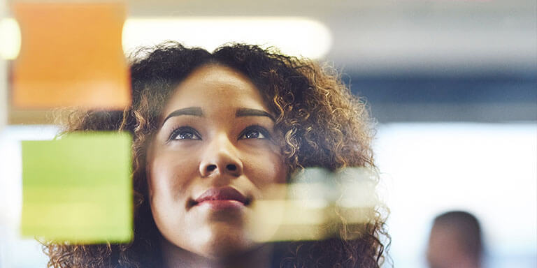 Businesswoman staring at a glass board covered in colored sticky notes