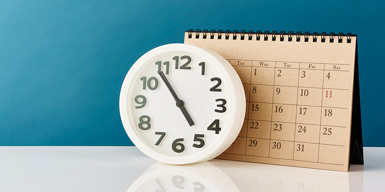 A white clock and a large construction paper calendar resting against a teal-colored wall