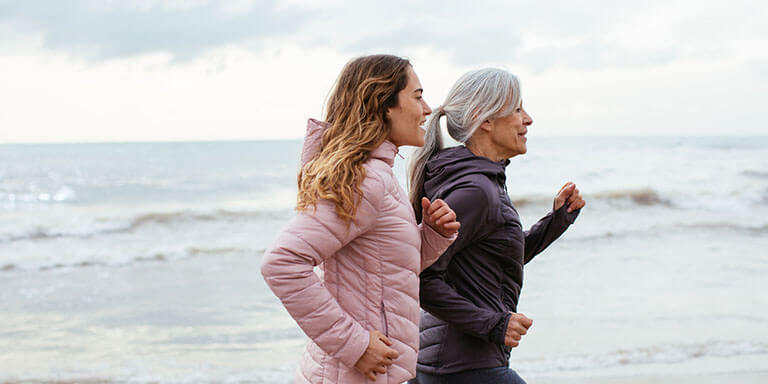 A woman and her mother in active wear running on a beach