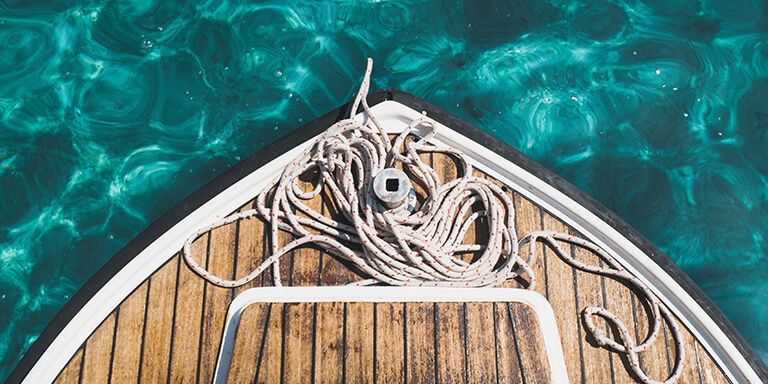 Overhead view of a coil of rope resting on the bow of a boat in clear turquoise water