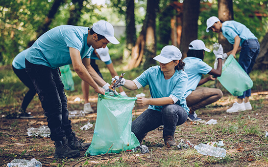 A group of volunteers wearing matching outfits picking up trash in the woods 