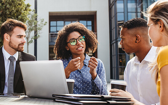 A group of young professionals engaging in discussion while drinking coffee and looking at a laptop computer