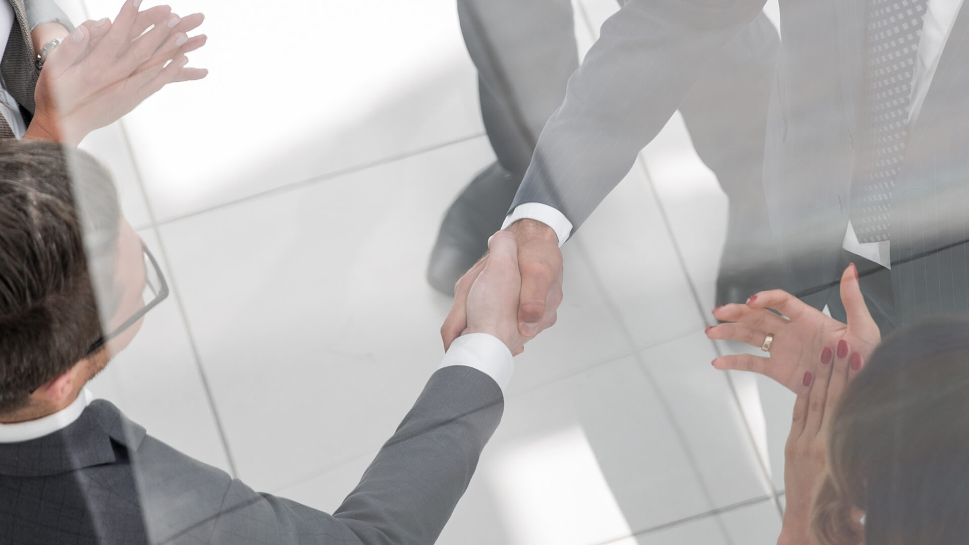 Two businessmen shaking hands while people clap around them