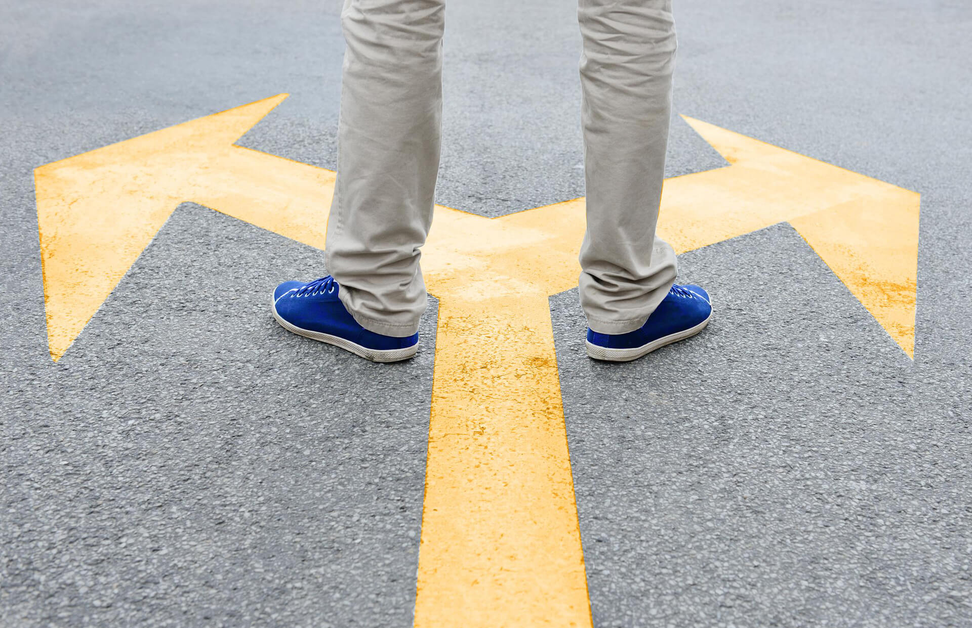 A man standing in front of a sign that indicates an upcoming fork in the road and has one foot on either side