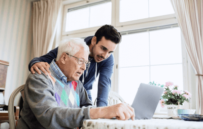 Caretaker and senior man using laptop in nursing home