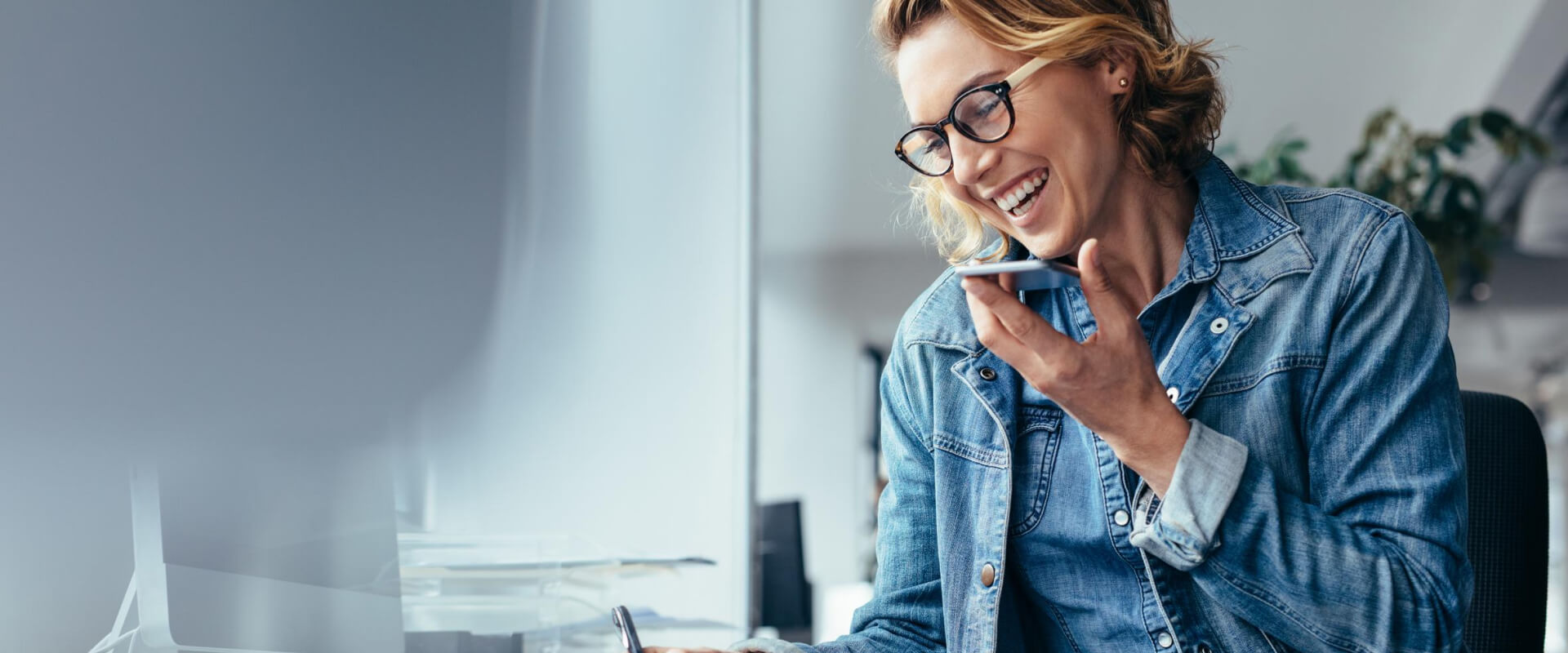 A woman laughing as she talks on the phone with someone while writing things down in a notebook