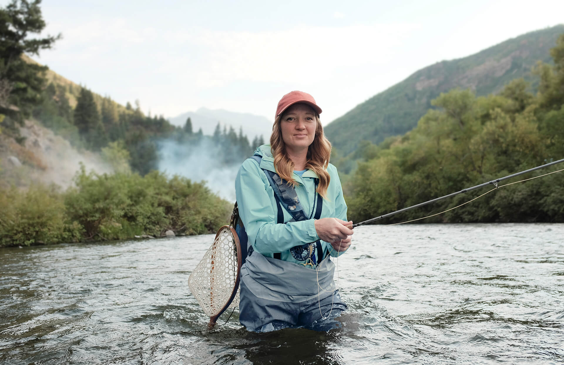 Woman in a hat and athletic clothes fly fishing in a river