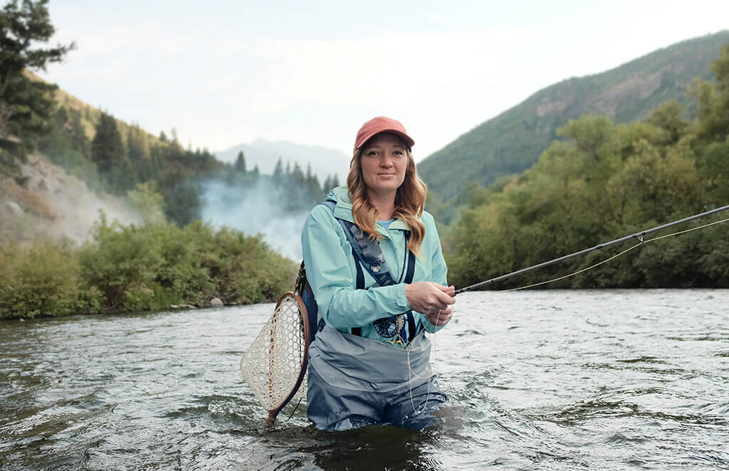 Woman in a hat and athletic clothes fly fishing in a river
