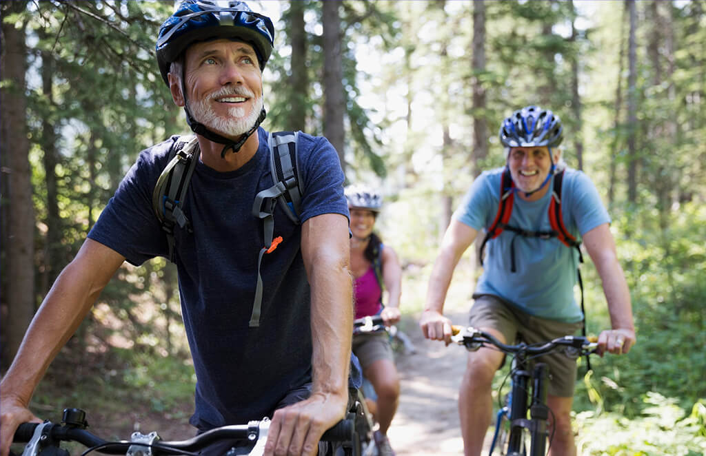 3 people in helmets riding their bikes through a forest trail