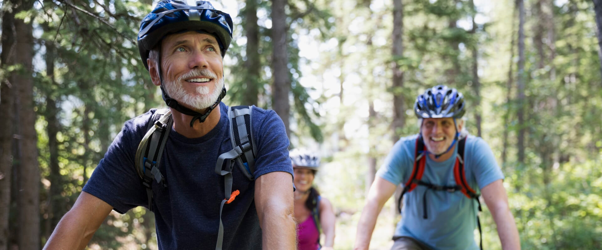 3 people in helmets riding their bikes through a forest trail