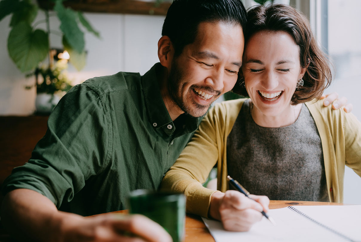 Smiling pair reviewing documents indoors, highlighting financial planning and retirement strategy for later life.