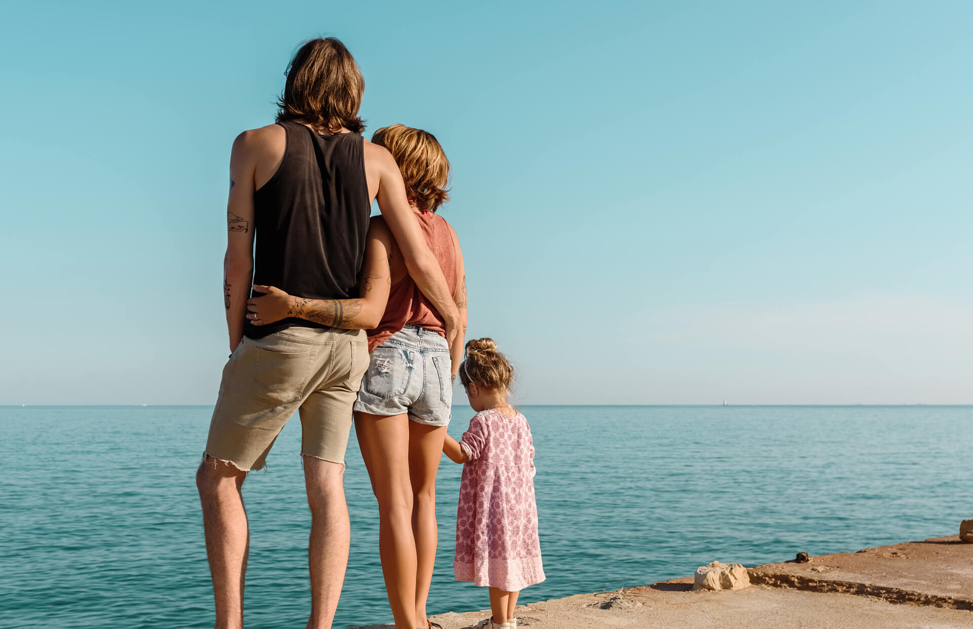 Embracing couple with their young daughter standing on concrete seafront in sunlight