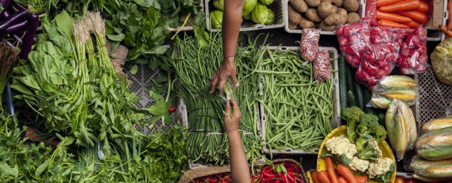 Overhead view of two people exchanges vegetables over a vegetable table in a market