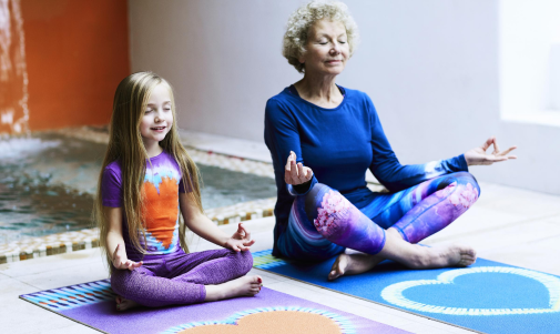 A young girl and her grandmother doing yoga together on mats in their living room