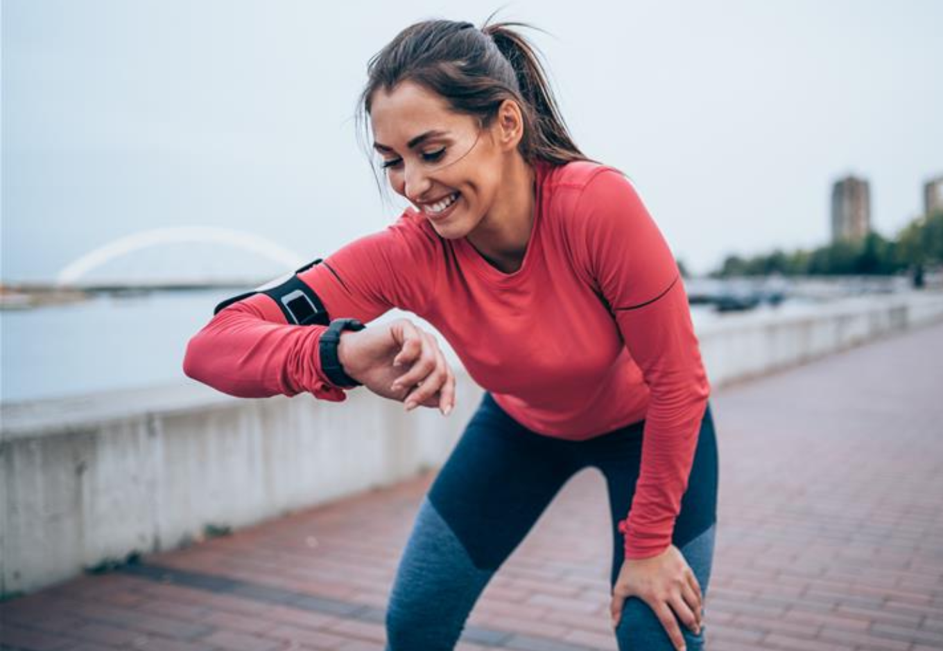 A woman smiling while checking her watch and measuring her blood pressure after a run.